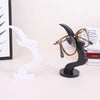 A black minimalist side face glasses holder with gold-rimmed glasses and a white stand.