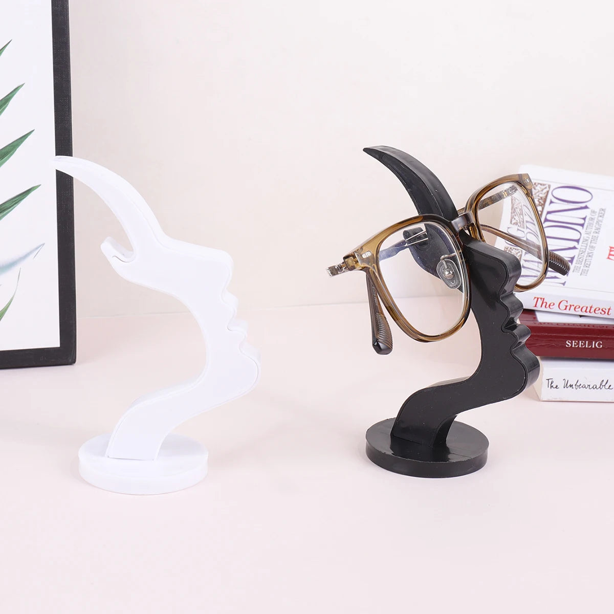 A black minimalist side face glasses holder with gold-rimmed glasses and a white stand.