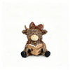 A cute coffee cow figurine with brown fur, large eyes, and a bow, resting on an open book.