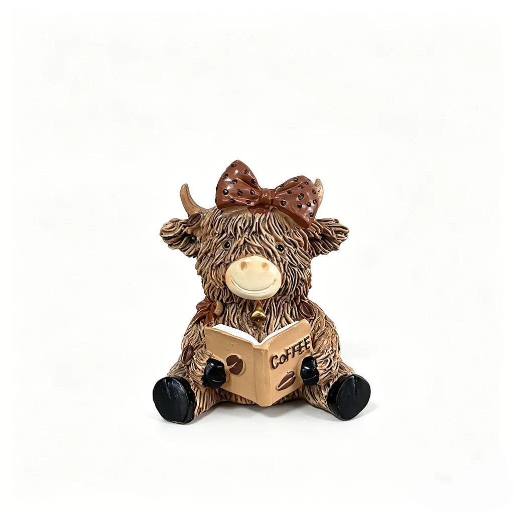 A cute coffee cow figurine with brown fur, large eyes, and a bow, resting on an open book.