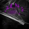 A dark spider decoration with glowing purple LED lights is suspended in a white web against a black background.