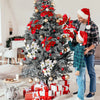 A man and a young boy decorating a Christmas tree with artificial poinsettia leaves and ornaments.
