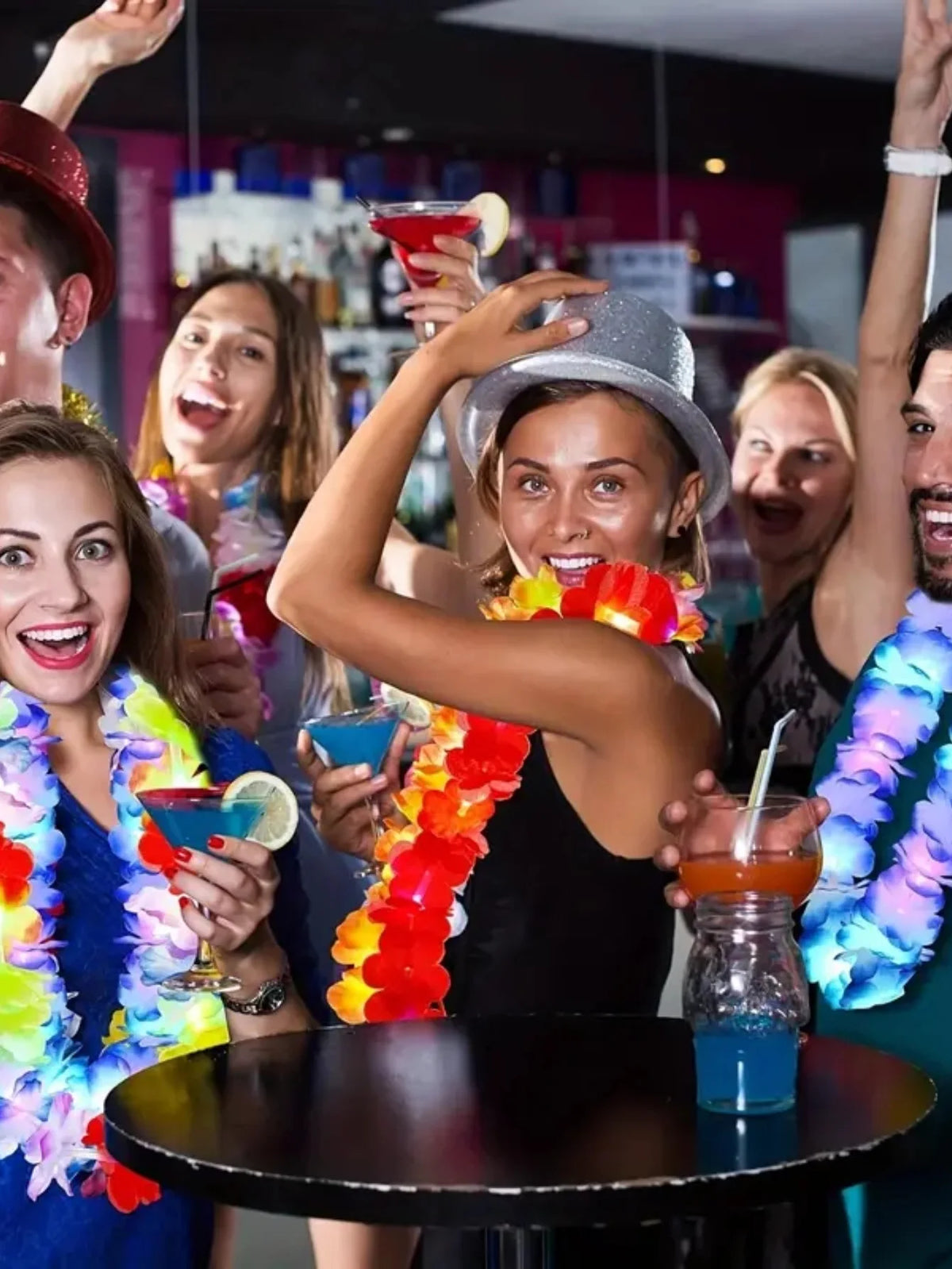 A group of people celebrating with glow-in-the-dark LED Hawaiian lei necklaces and colorful drinks.