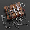 A collection of realistic miniature alloy gun models on a wooden surface, attached to various metal keychains.