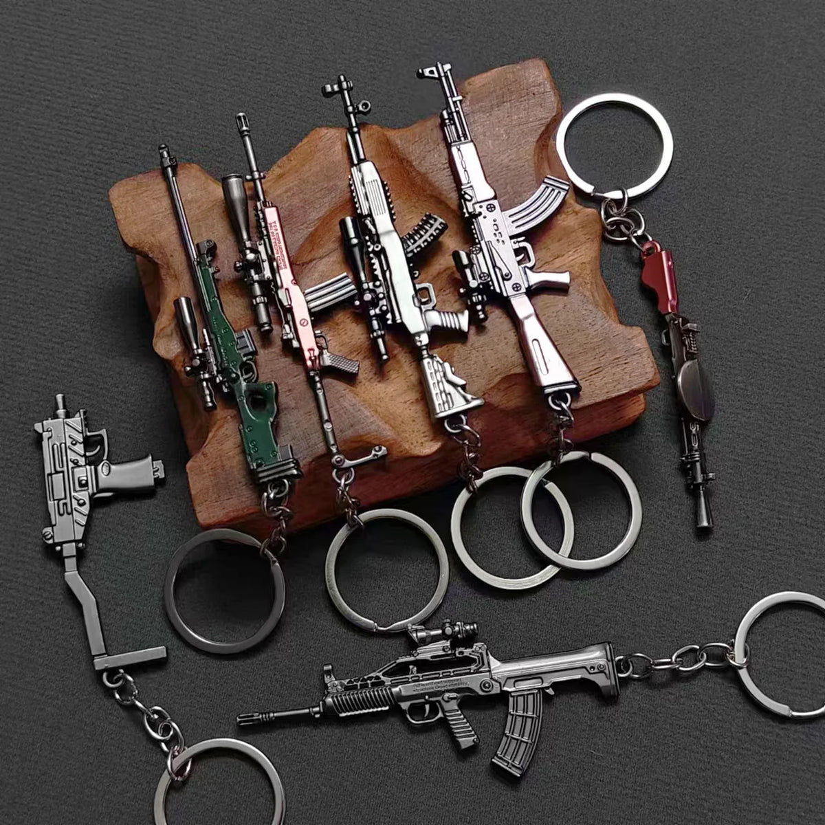 A collection of realistic miniature alloy gun models on a wooden surface, attached to various metal keychains.