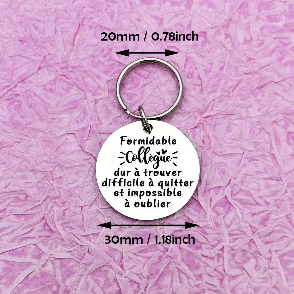 A round white keychain with a silver ring engraved with the French quote Formidable collègue dur à trouver et impossible à ou