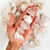 A hand holds a pile of natural raw pink quartz crystal stones for healing and decoration.