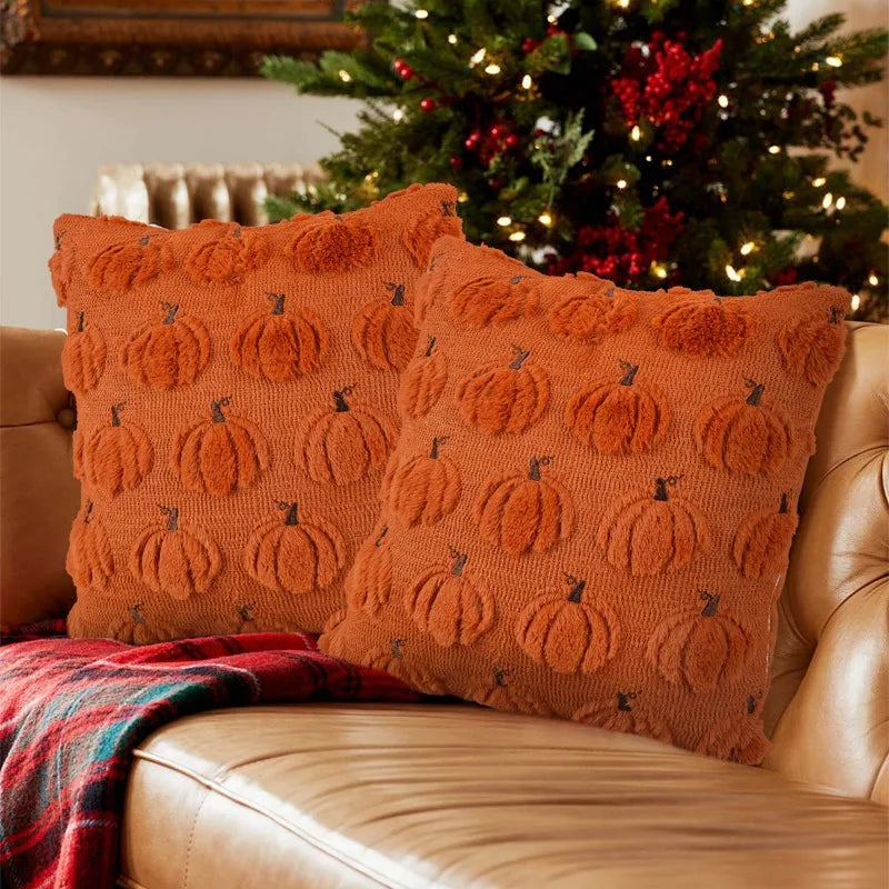 Two orange plush pumpkin ghost pillow covers resting on a leather sofa in front of a decorated Christmas tree.
