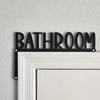 Black metal sign spelling out BATHROOM mounted on a white door frame