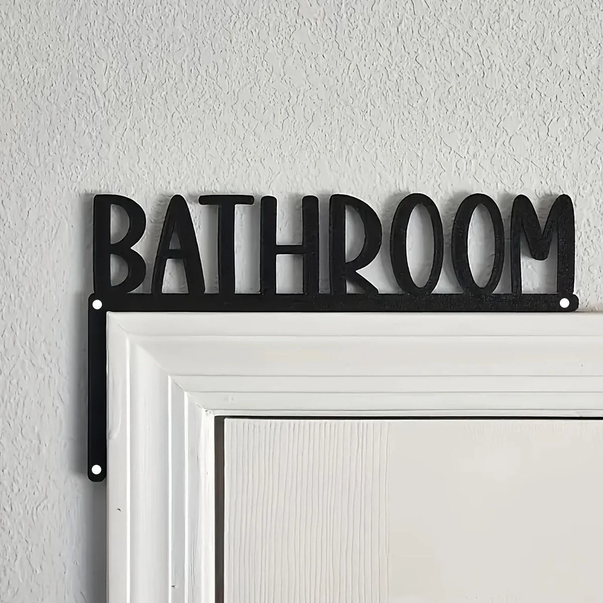 Black metal sign spelling out BATHROOM mounted on a white door frame