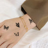 A hand displaying realistic black butterfly temporary tattoos on the wrist, next to a brown blazer sleeve.