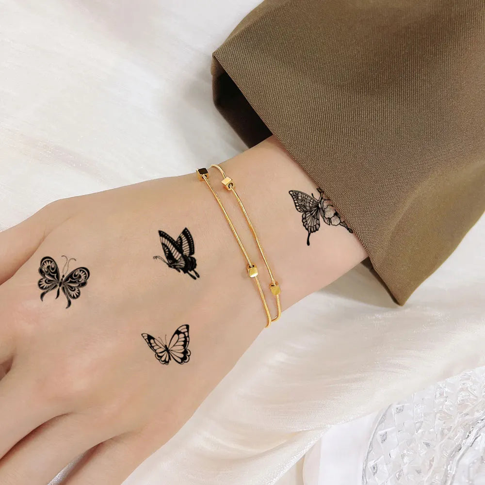 A hand displaying realistic black butterfly temporary tattoos on the wrist, next to a brown blazer sleeve.