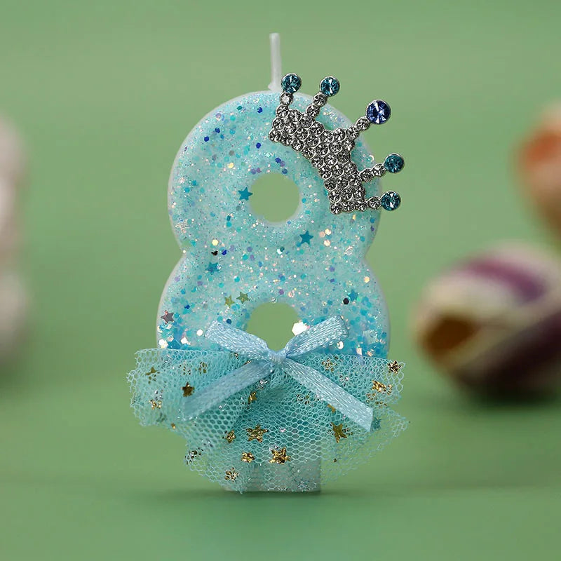 A light blue glitter birthday candle decoration shaped like the number 8 with a silver crown and a sheer blue ribbon skirt.