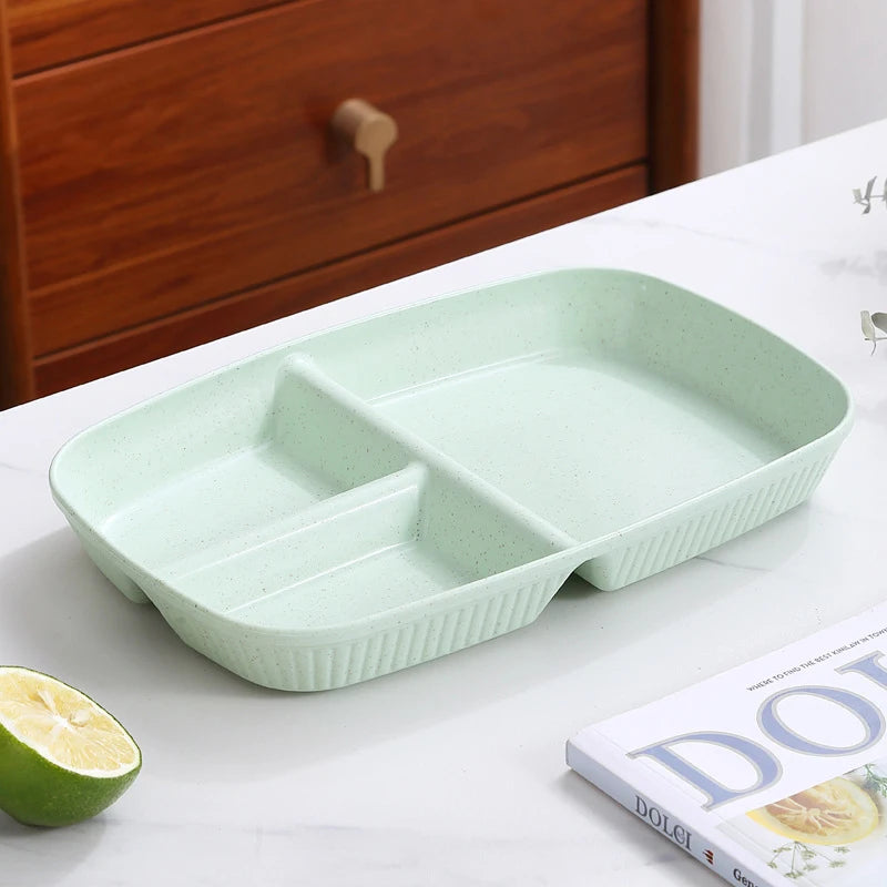 A light green 3-compartment portion control plate is displayed on a white surface next to a lime slice and a book.