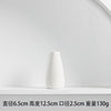 A white ceramic vase with a tapered shape is displayed on a white shelf.