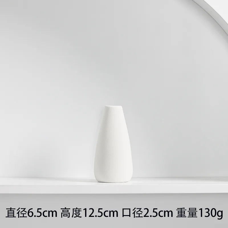 A white ceramic vase with a tapered shape is displayed on a white shelf.