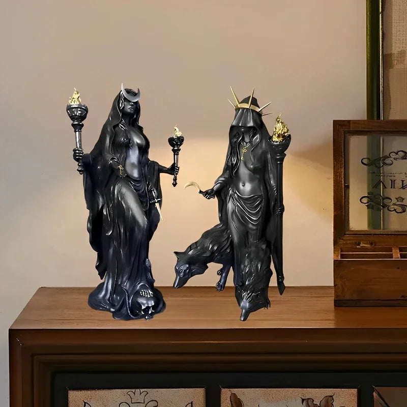 A dark resin statue of a goddess with horns and mystical details, standing next to a reclining figure.