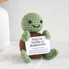 A handmade plush knitting doll shaped like a green turtle sitting on a white surface.