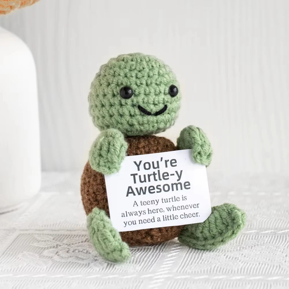 A handmade plush knitting doll shaped like a green turtle sitting on a white surface.