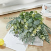 A lush bouquet of mixed green eucalyptus and willow artificial flowers displayed on a white paper.