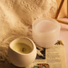 A clear silicone arc candle jar is shown resting on a textured white fabric next to a printed page.