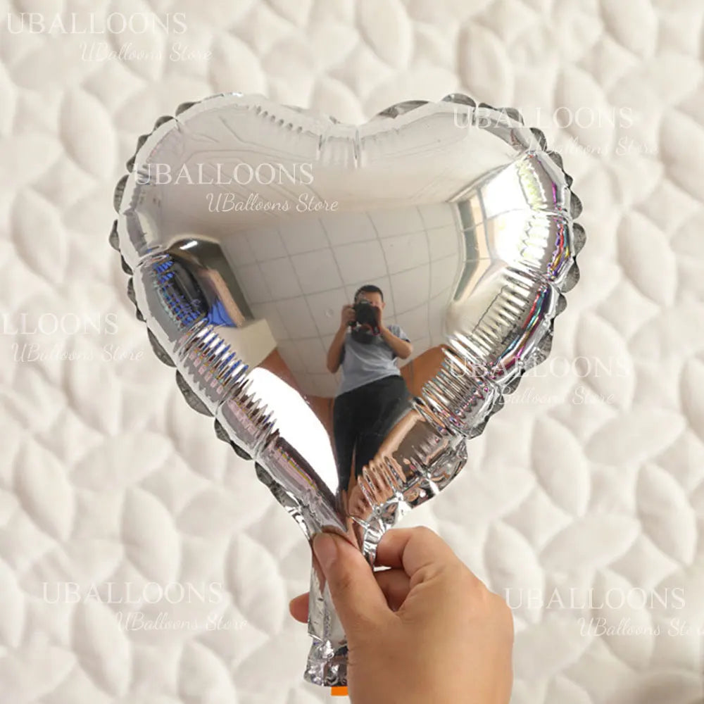 A silver heart-shaped foil balloon is held up by a person against a white quilted background.