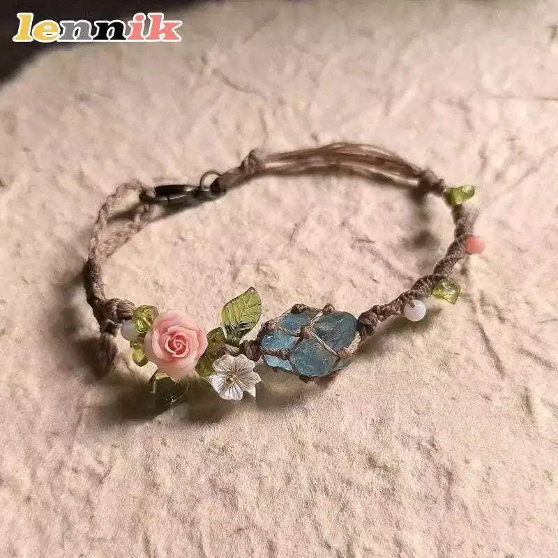 A macrame bracelet featuring raw aquamarine beads and a pink rose accent, tied with natural twine.
