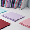 A collection of colorful spiral-bound paper scrapbooks and a plain purple notebook are displayed on a white surface.