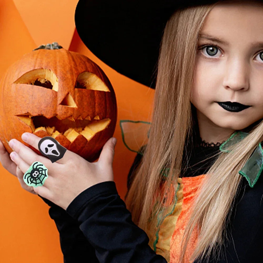 A young girl wearing a witch costume holds an orange carved pumpkin and glow-in-the-dark Halloween rings.