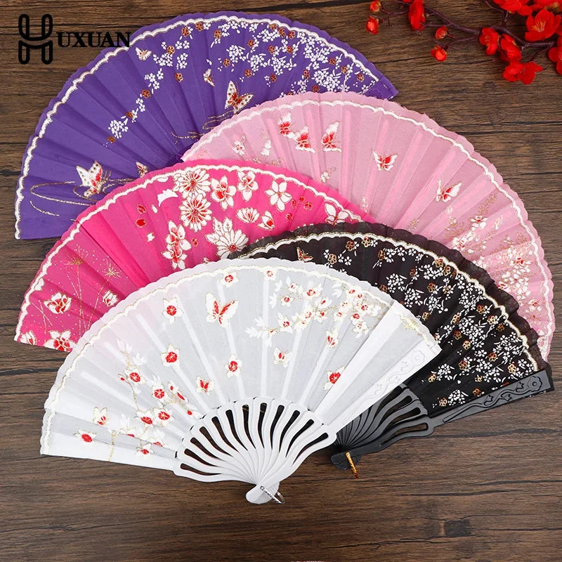 A collection of five folding fans in various shades of pink, purple, and black with floral patterns.
