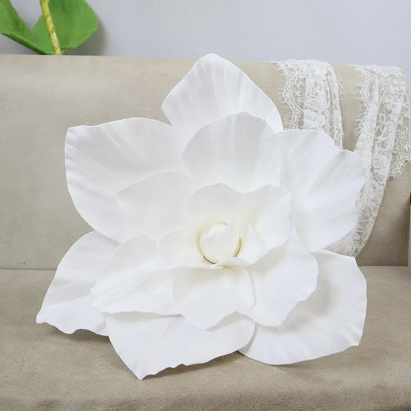 A large white PE foam rose flower displayed on a beige sofa next to white lace fabric.