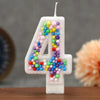 A white birthday candle shaped like the number 4 decorated with colorful candy beads