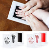 A hand is pressing a handprint onto a framed piece of paper, demonstrating an inkless baby keepsake kit.