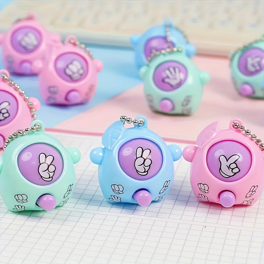 A collection of colorful mini rock-paper-scissors themed keychains in pink, purple, and teal resting on a white grid.