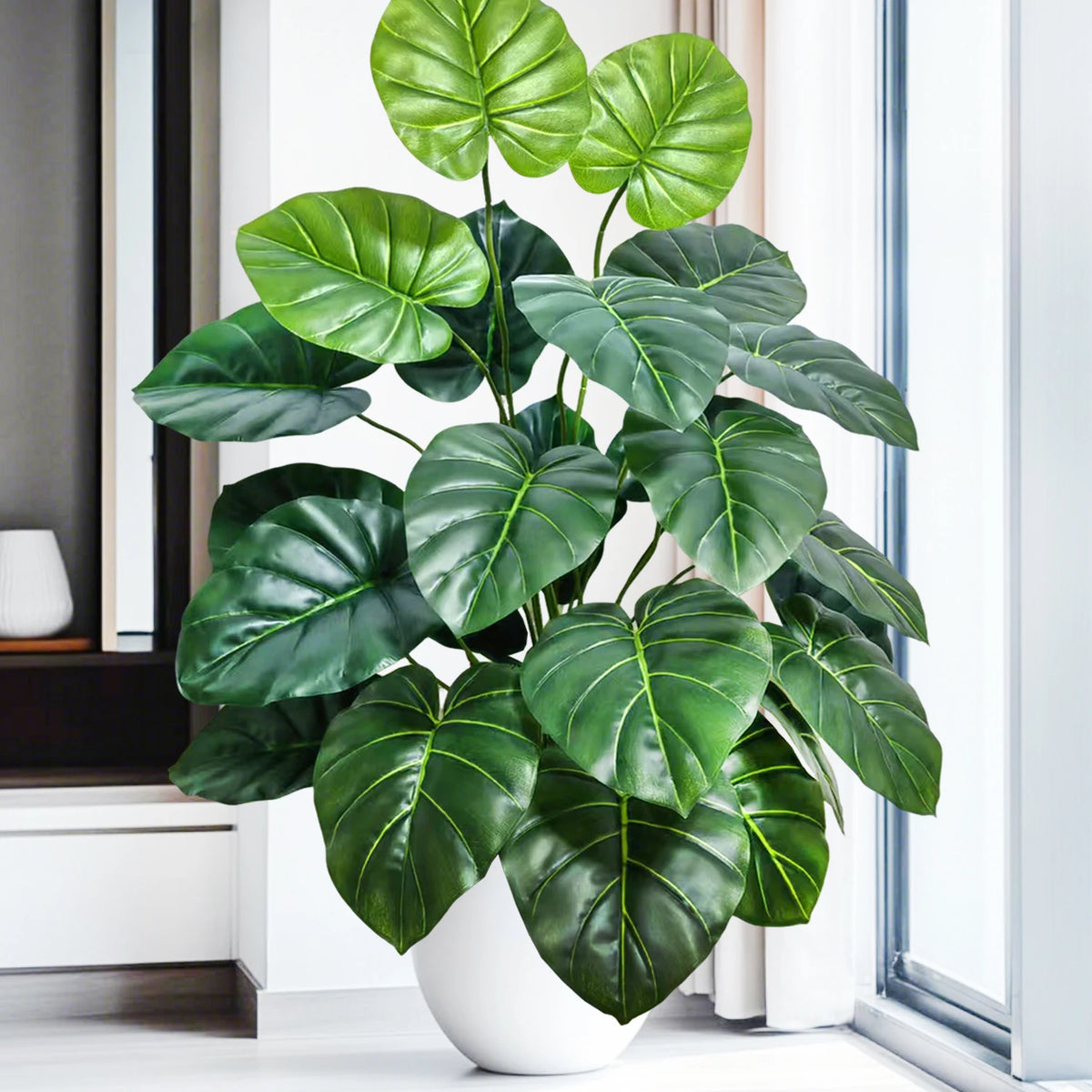 A vibrant artificial monstera plant with large green silk leaves displayed in a white pot near a window.