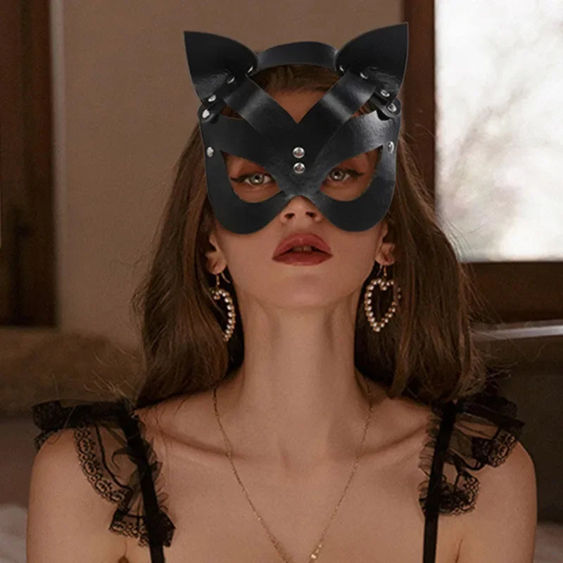 A model wearing an elegant black fox masquerade mask with silver studs and a delicate gold necklace.