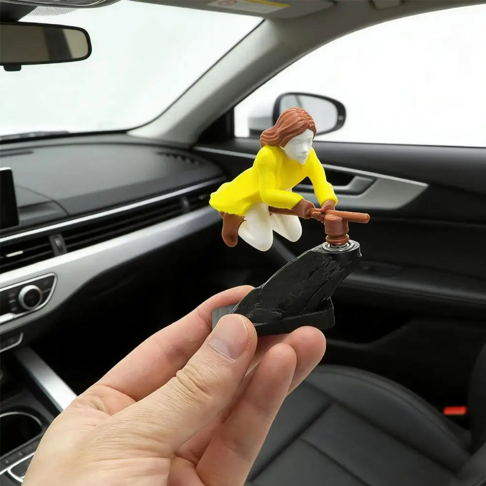A small figurine of a witch and wizard flying carriage is held by a hand in the interior of a car dashboard.