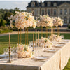 A long table decorated with silk champagne rose and hydrangea flower ball centerpieces for an event.