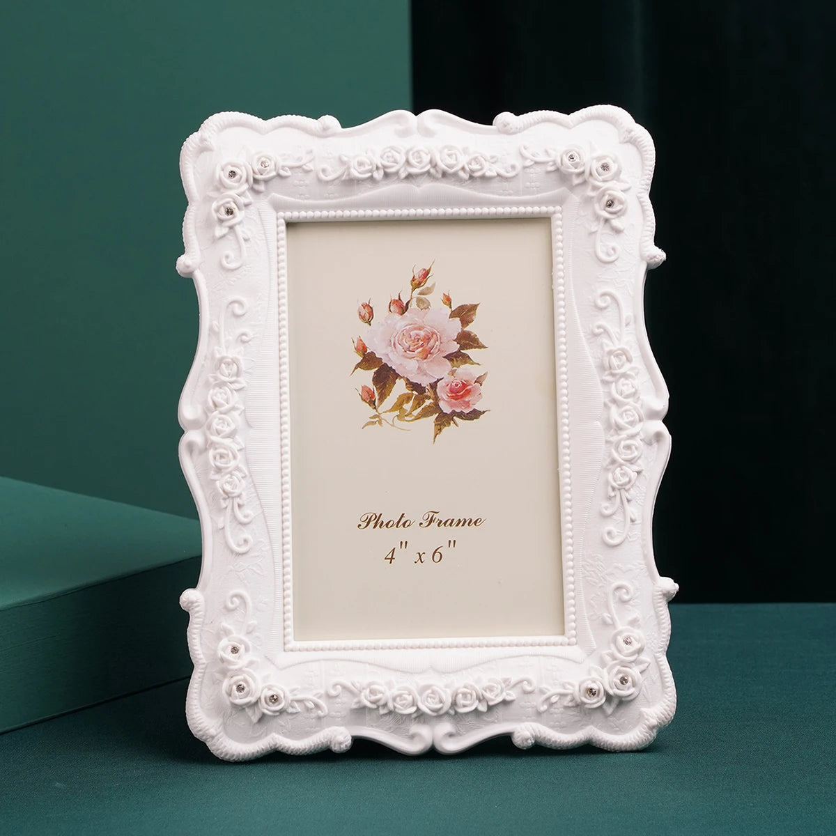 A white, ornate resin photo frame with a floral embossing, displayed on a dark green surface.