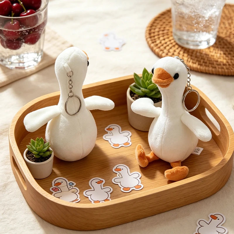 A white duck plush keychain pendant resting on a wooden tray with small cutout shapes.