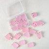 A collection of pink glow-in-the-dark resin pig decorations in a clear plastic container and scattered on a white surface.