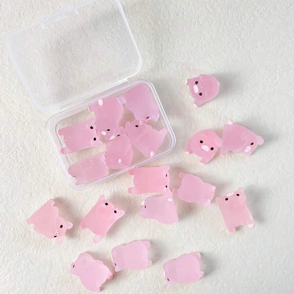 A collection of pink glow-in-the-dark resin pig decorations in a clear plastic container and scattered on a white surface.