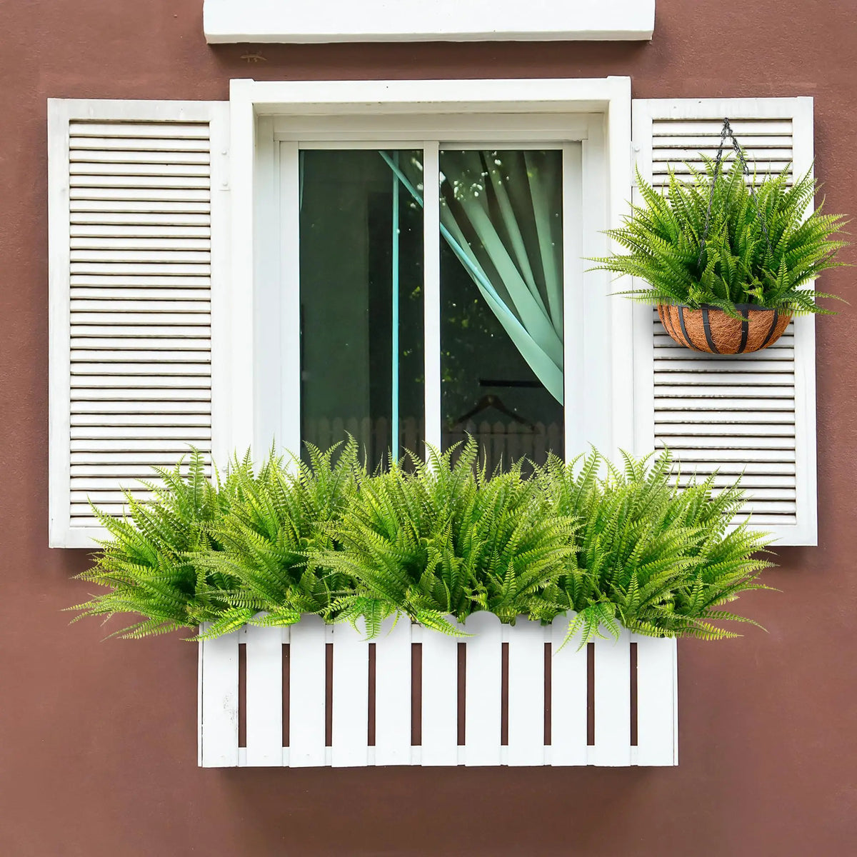 Two artificial Boston fern bushes in terracotta pots displayed in a white window box on a brown wall.