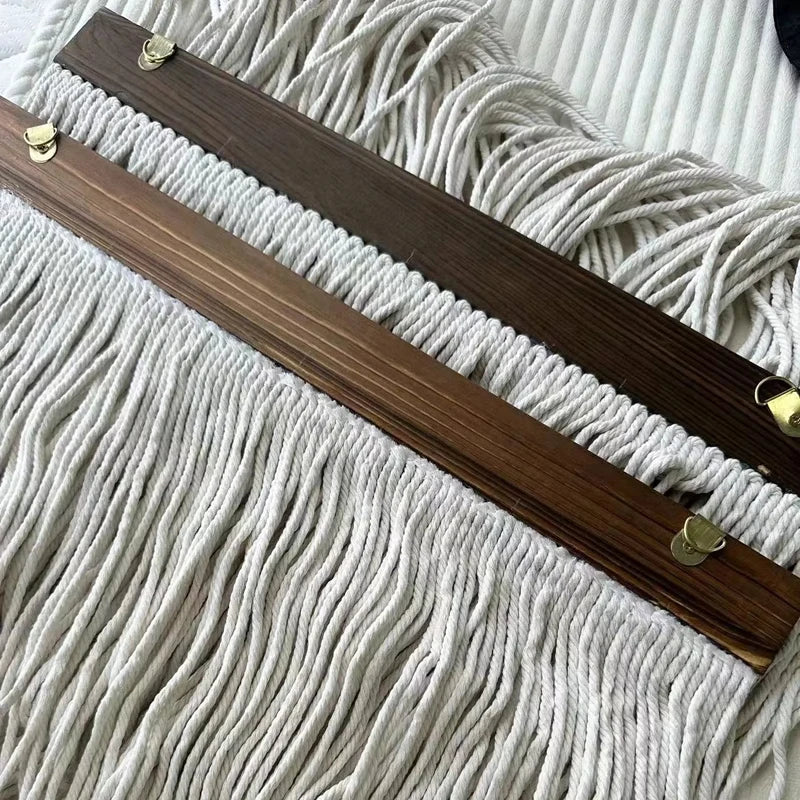 A dark brown wooden dowel with brass hardware is laid diagonally across a light beige macrame textile.