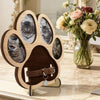 A wooden paw print frame with slots for pet photos and a leather collar hanging from it.