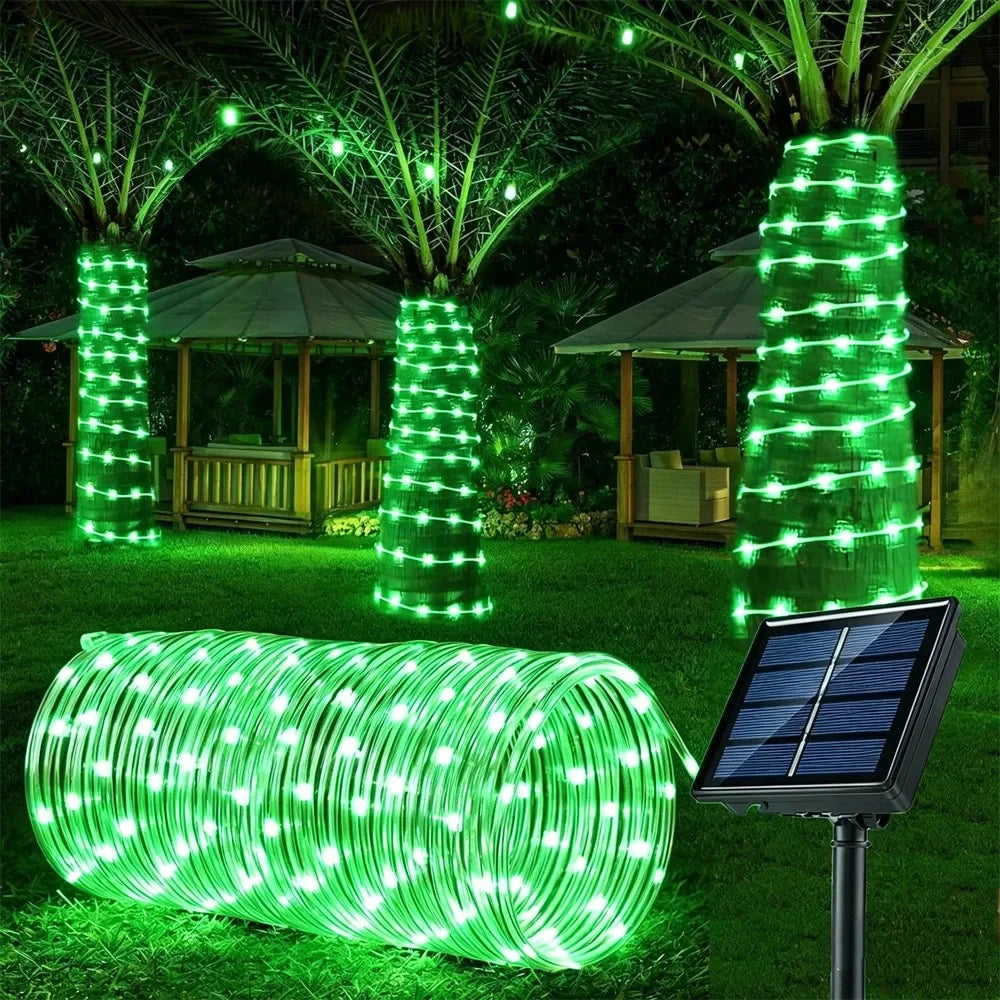 A coiled green LED rope light illuminates a garden scene with surrounding trees and structures.