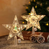 A sparkling LED Christmas tree star topper with a warm white glow displayed on a dark surface.