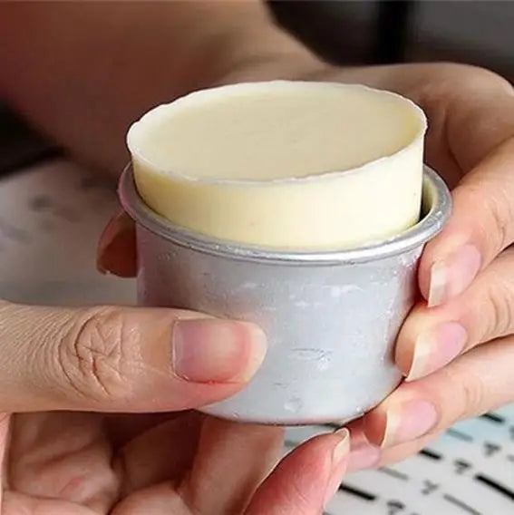 A hand holds a light yellow non-stick round cake mold with a removable base.