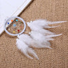 A handmade feather dreamcatcher with a circular hoop and white feathers rests on a beige woven fabric.