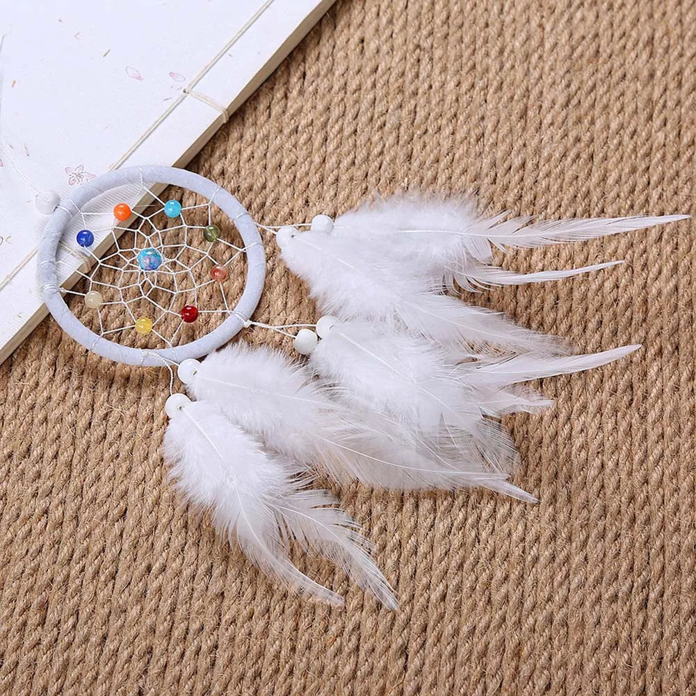 A handmade feather dreamcatcher with a circular hoop and white feathers rests on a beige woven fabric.